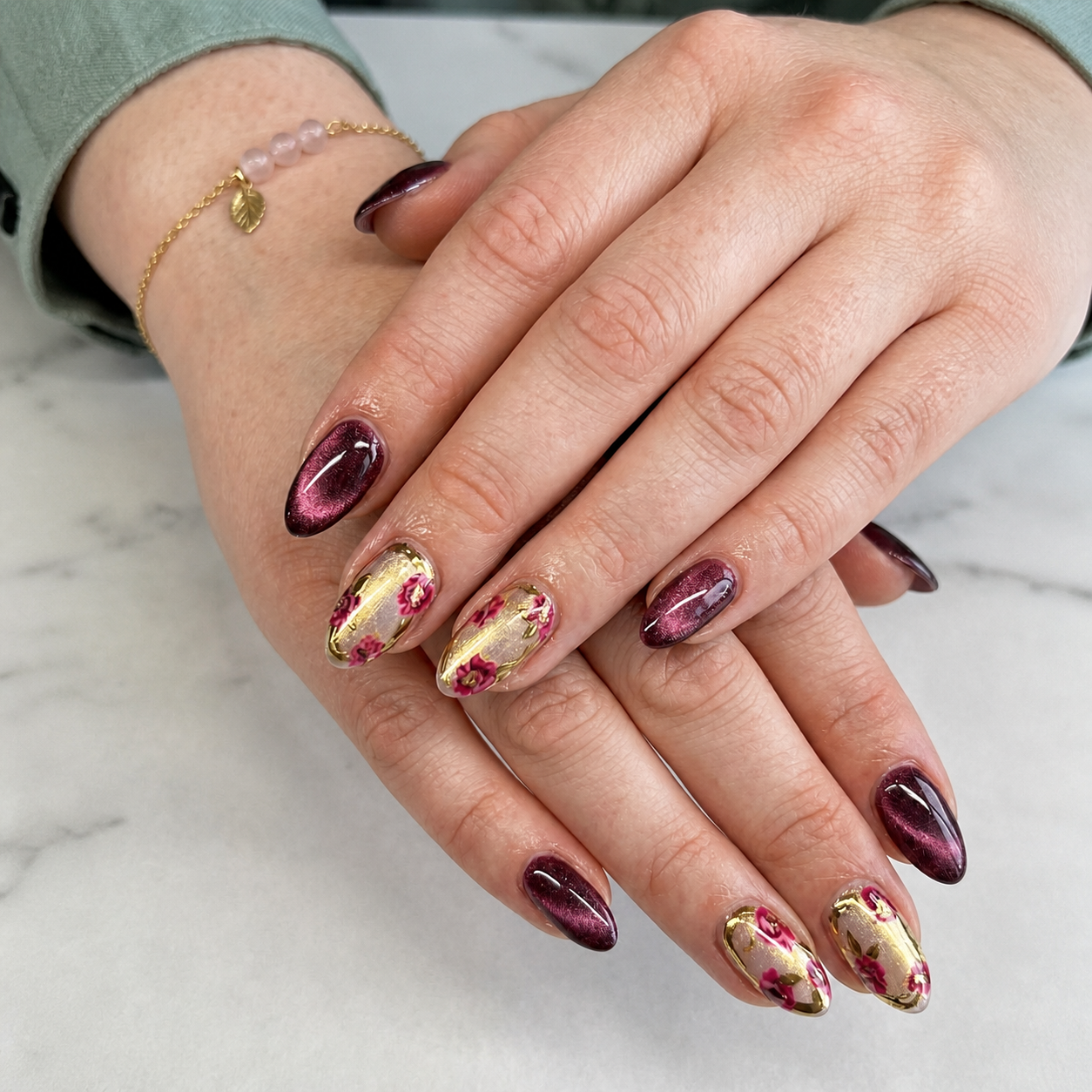 Burgundy cat-eye manicure with floral gold accent nails